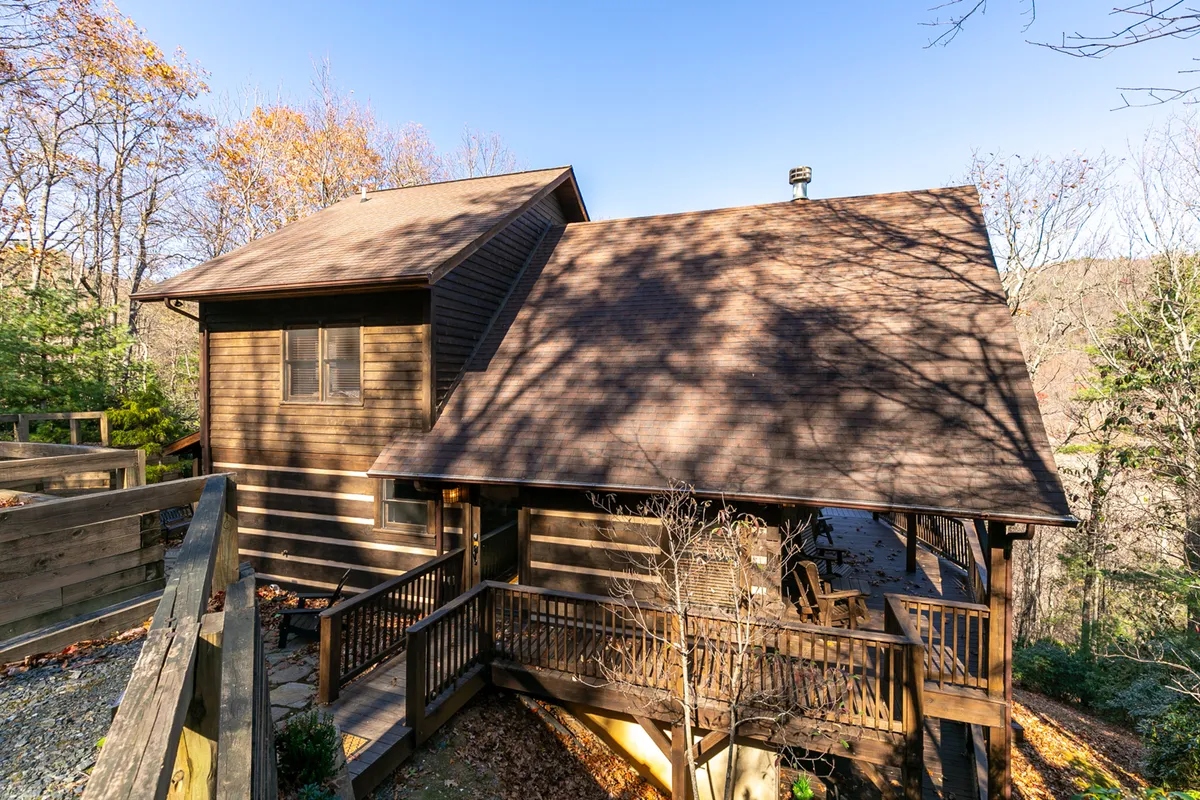 This image captures the exterior of the cabin featuring a wooden balcony, sloping roof, and surrounding trees, with an inviting deck area ideal for family gatherings or outdoor relaxation.