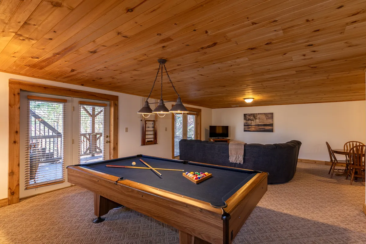 A well-lit entertainment area featuring a pool table, a plush sofa, a dining table, and large windows that bring in natural light. The layout encourages group interactions, whether playing games, dining, or relaxing. The atmosphere feels welcoming and flexible.