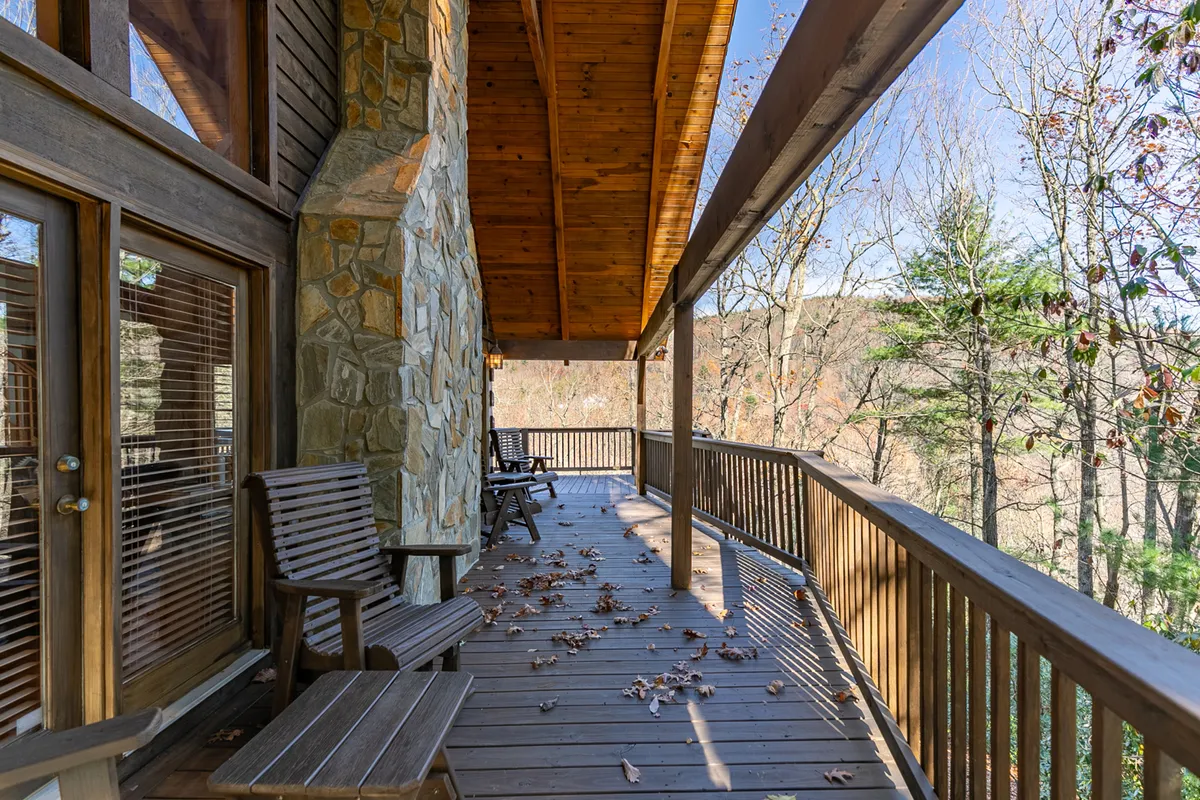 A wooden deck with rocking chairs overlooks the surrounding trees, inviting relaxation and time spent outdoors. The tranquil atmosphere is ideal for unwinding after an active day and blends the comforts of home with the beauty of nature.