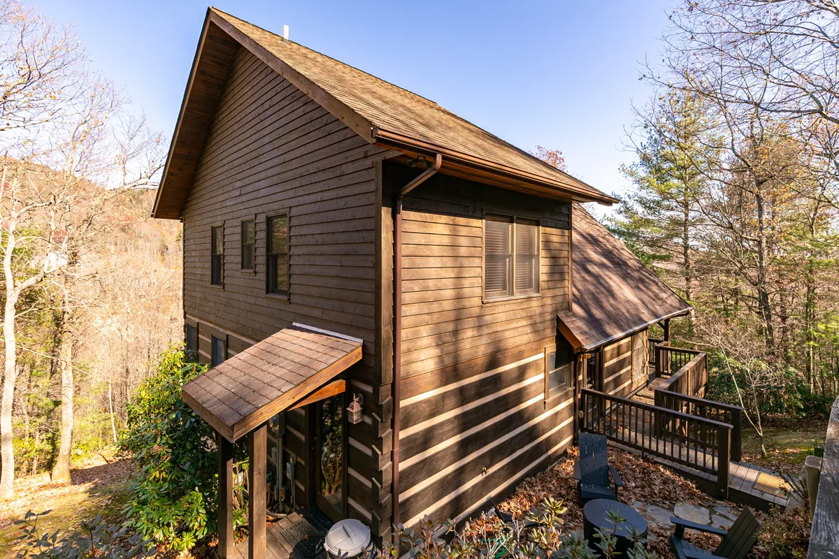 A serene exterior shot of the cabin's wooden façade, surrounded by tall trees and showcasing a large deck area—ideal for enjoying nature and family gatherings.