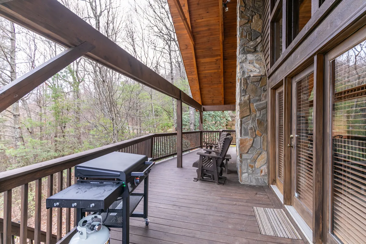 A wooden deck with rocking chairs and a grill, set against a lush natural landscape. The setting is calm and inviting, ideal for outdoor meals, morning coffee, or simply soaking in the peacefulness of the mountain air.