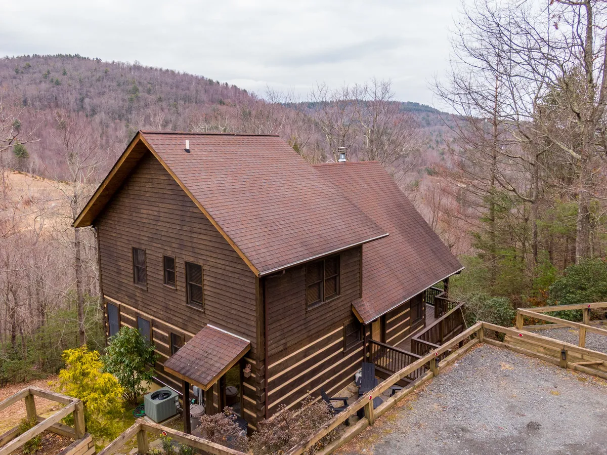 A tranquil log cabin set amidst tall trees with a stunning mountain backdrop. The porch invites relaxation, hinting at activities like sipping morning coffee or winding down after a day exploring. The natural setting is peaceful, emphasizing the cabin’s proximity to adventure and the serenity of the mountain environment.