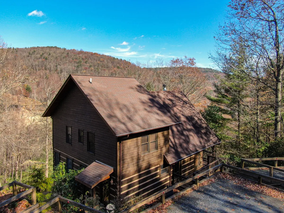 The exterior of the wooden house is framed by mature trees and a gravel driveway, visually connecting the home to its natural surroundings and illustrating the peaceful, welcoming entry point for both guests and pets.