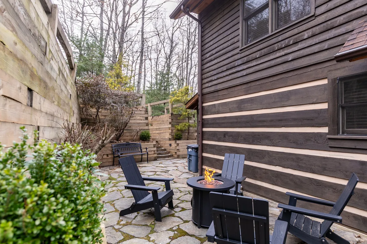 An inviting fire pit area with wooden chairs and a stone pathway sits nestled among trees, offering a cozy spot for evening gatherings, storytelling, and outdoor relaxation. The fire pit is central, surrounded by ample seating, making it ideal for group activities.